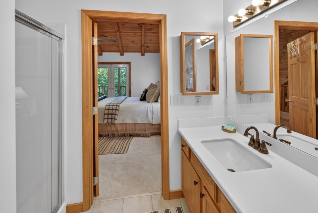 Modern bathroom with dual sinks and wooden accents, leading to a cozy bedroom with forest views.