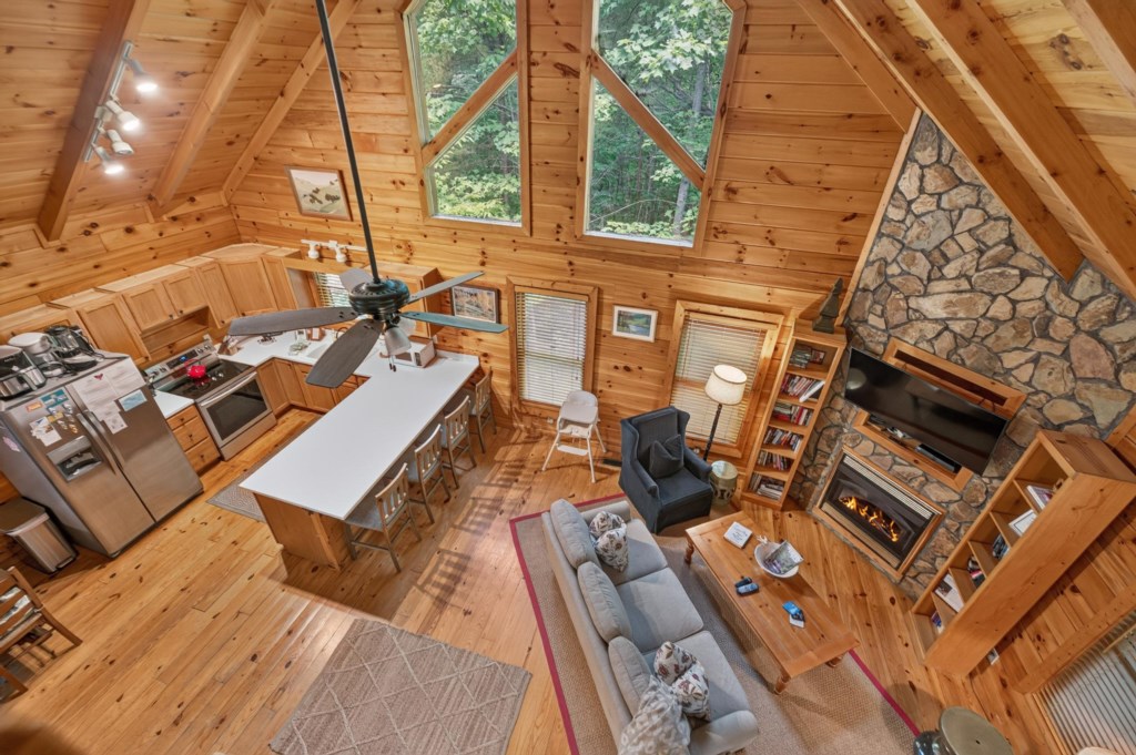 Rustic open-concept living area with stone fireplace and forest views.