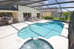 Screened-in pool with hot tub, patio furniture, and lush garden views.