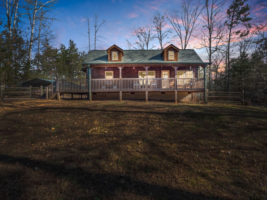 Charming log cabin with a spacious deck, perfect for enjoying serene forest views at sunset.