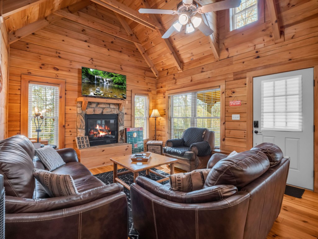 Cozy cabin living room with leather sofas, stone fireplace, and vaulted wooden ceiling.