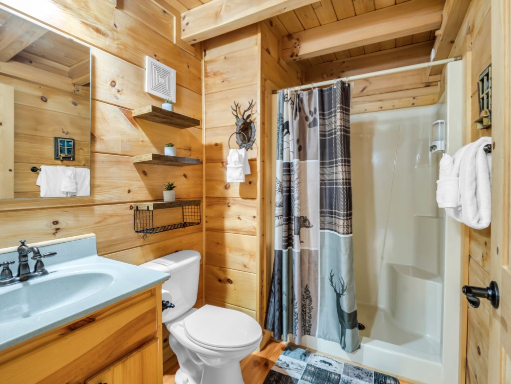 Rustic bathroom with wooden walls and a cozy shower, perfect for a cabin retreat.