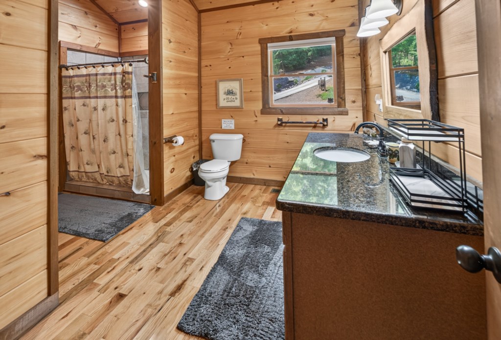 Rustic bathroom with wood paneling, granite countertop, and a cozy shower curtain.