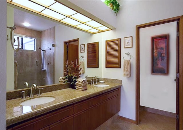 Brightly lit bathroom featuring dual sinks, a large mirror, and a spacious glass shower enclosure.