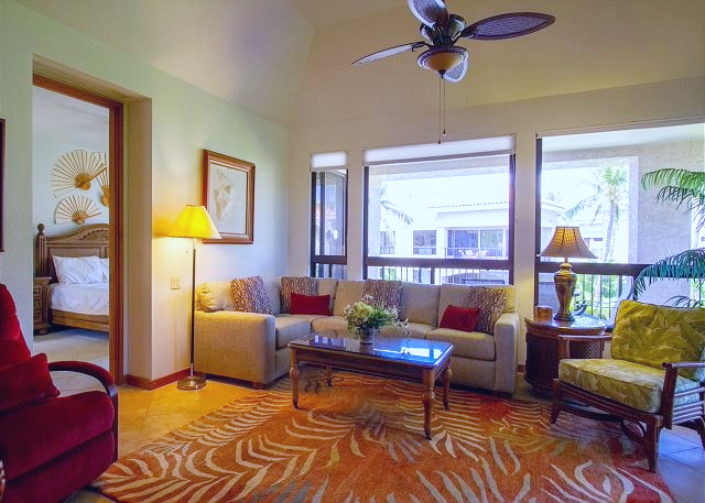 Relax in this inviting living room with tropical décor, abundant natural light, and views of lush greenery outside.