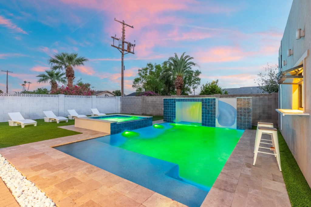 Modern pool with waterfall feature and sun loungers, perfect for relaxing evenings.