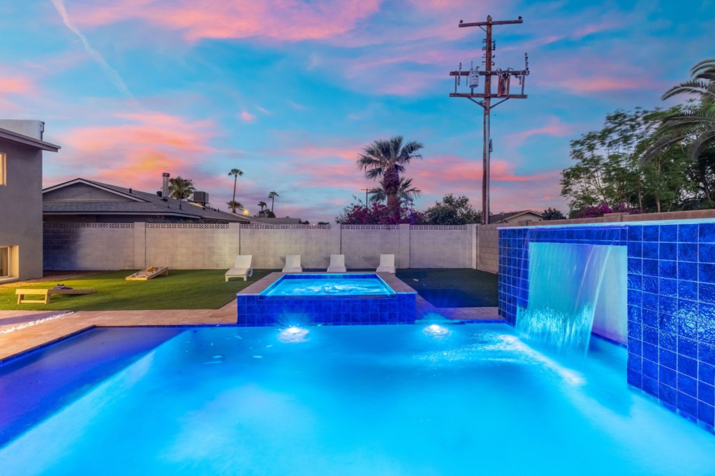 Relax by the illuminated pool with a cascading waterfall and sunset views.
