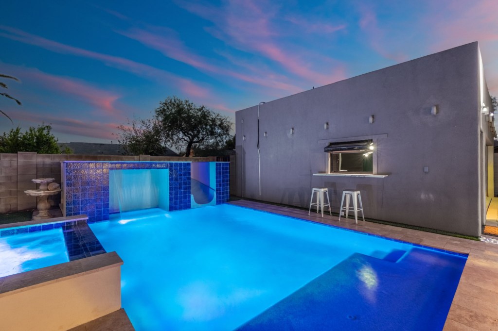 Modern pool with waterfall feature and poolside bar, perfect for evening relaxation.