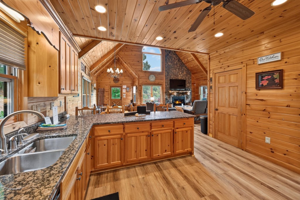 Rustic open kitchen with granite countertops and cozy living area with stone fireplace.