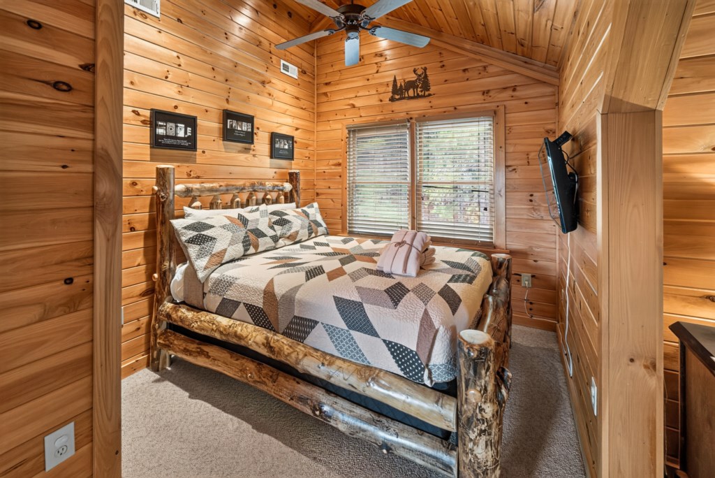Cozy cabin bedroom with rustic log bed and forest views through large windows.