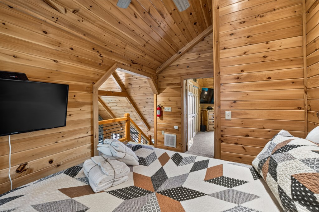 Cozy loft bedroom with rustic wood paneling and a flat-screen TV for ultimate relaxation.