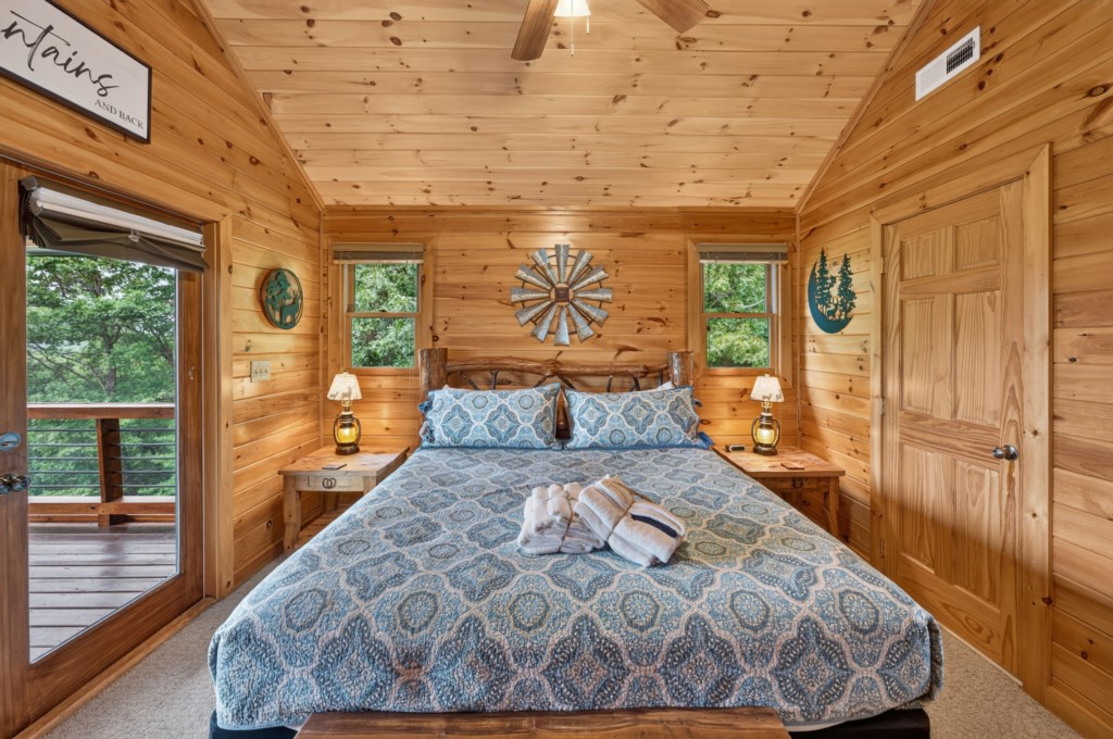 Cozy cabin bedroom with king bed and private balcony overlooking lush forest views.