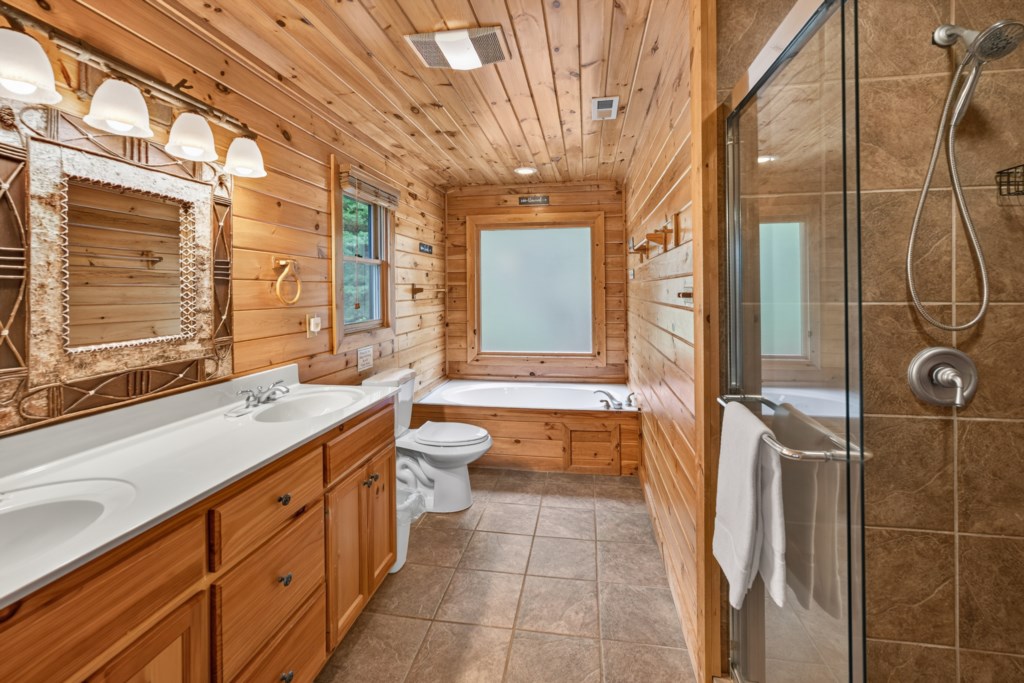 Rustic bathroom with dual sinks, jacuzzi tub, and a glass-enclosed shower.