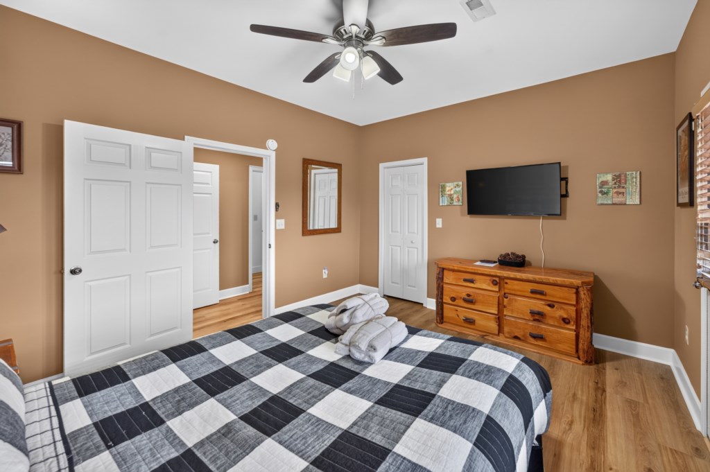 Cozy bedroom with a plaid bedspread, flat-screen TV, and wooden dresser.