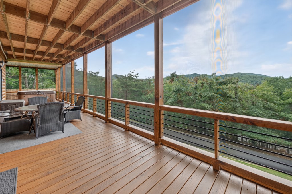 Spacious screened-in deck with hot tub and dining area, offering stunning mountain views.