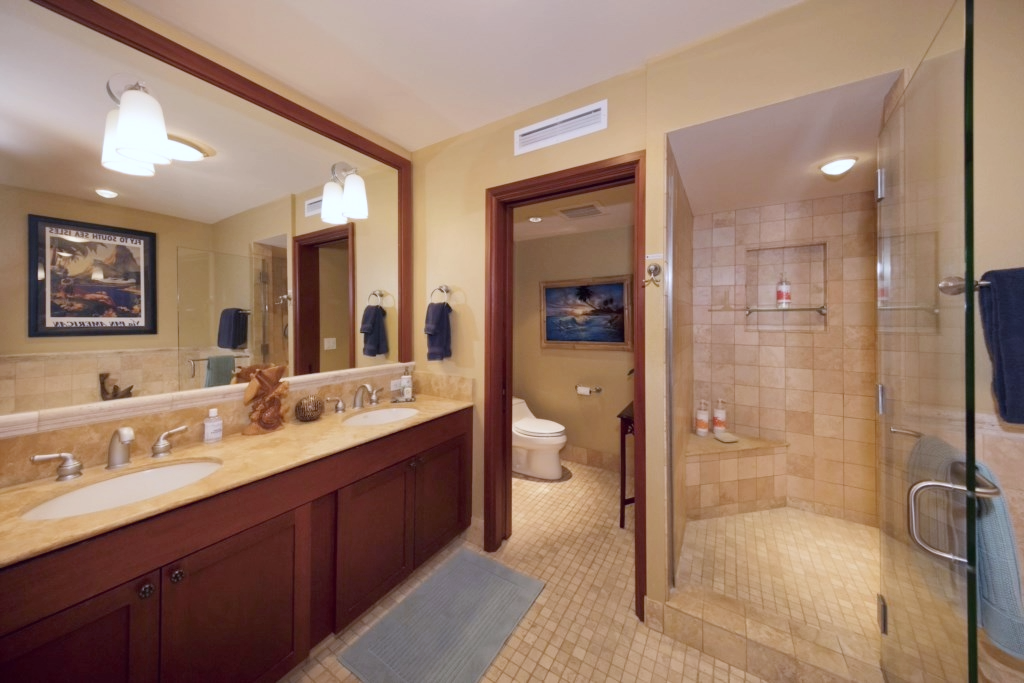 Stylish bathroom with walk in shower, dual sinks, elegant mirrors, and warm-toned tile finishes.