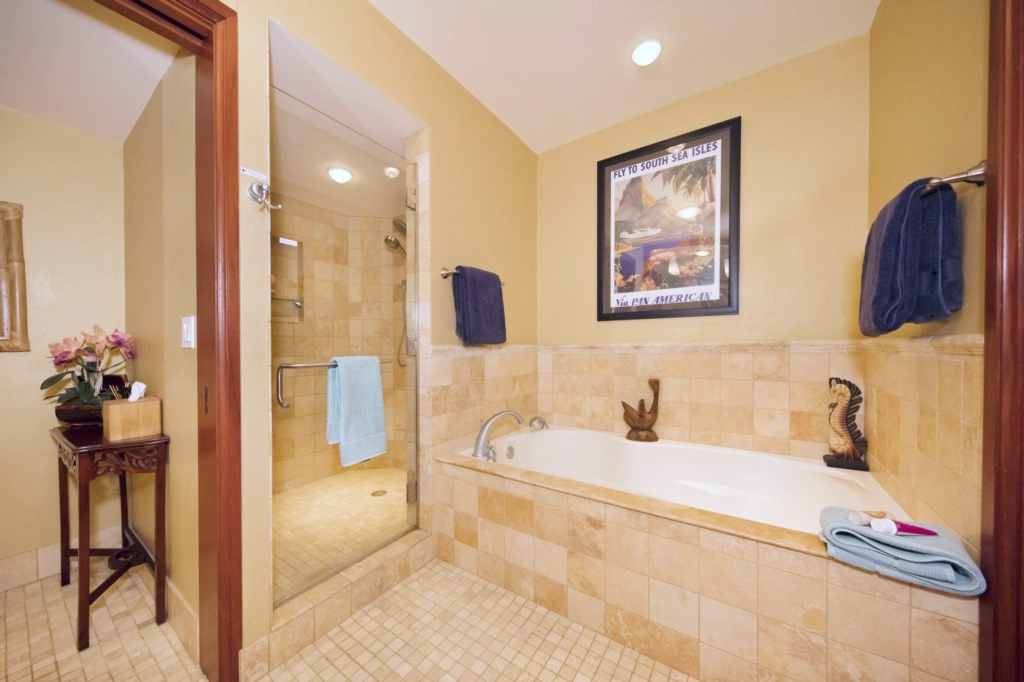 Spa style soaking tub framed in tile with island art above and nearby glass enclosed shower area.