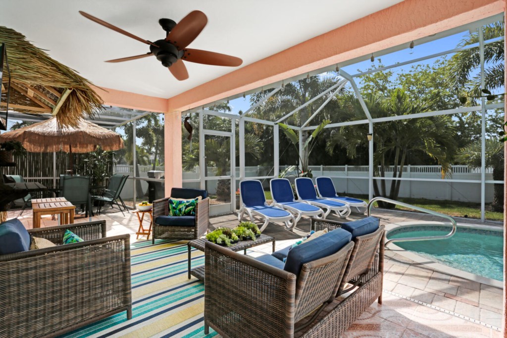 Tropical lanai with pool, lounge chairs, and tiki-style seating for relaxing in paradise.