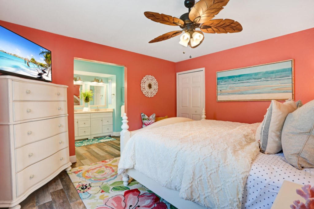 Colorful bedroom with ensuite bath, ceiling fan, and beach-themed decor.