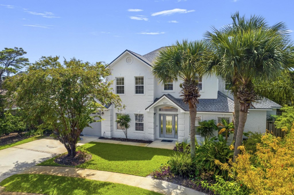 Elegant two-story vacation home surrounded by lush gardens and palm trees.