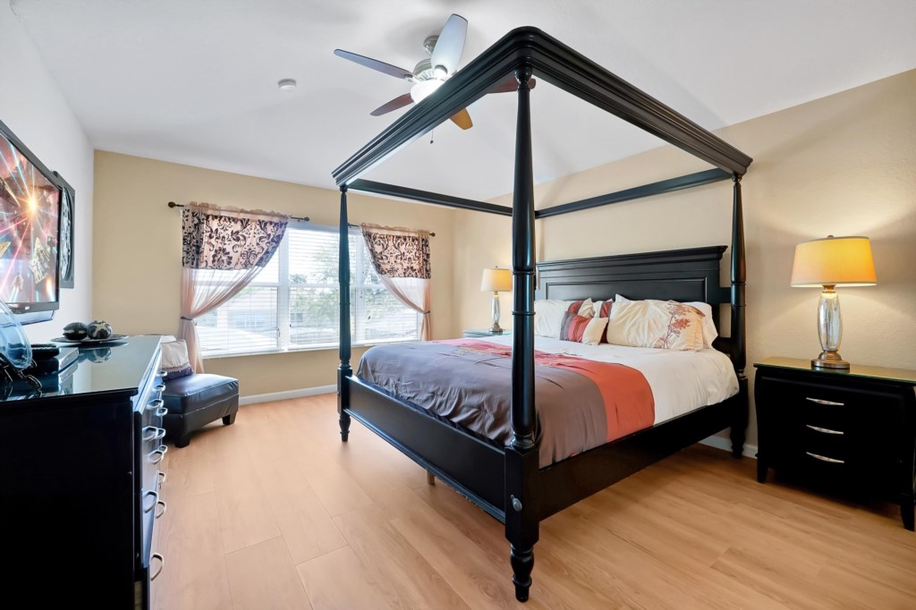 Elegant bedroom with a king canopy bed and natural light from large windows.