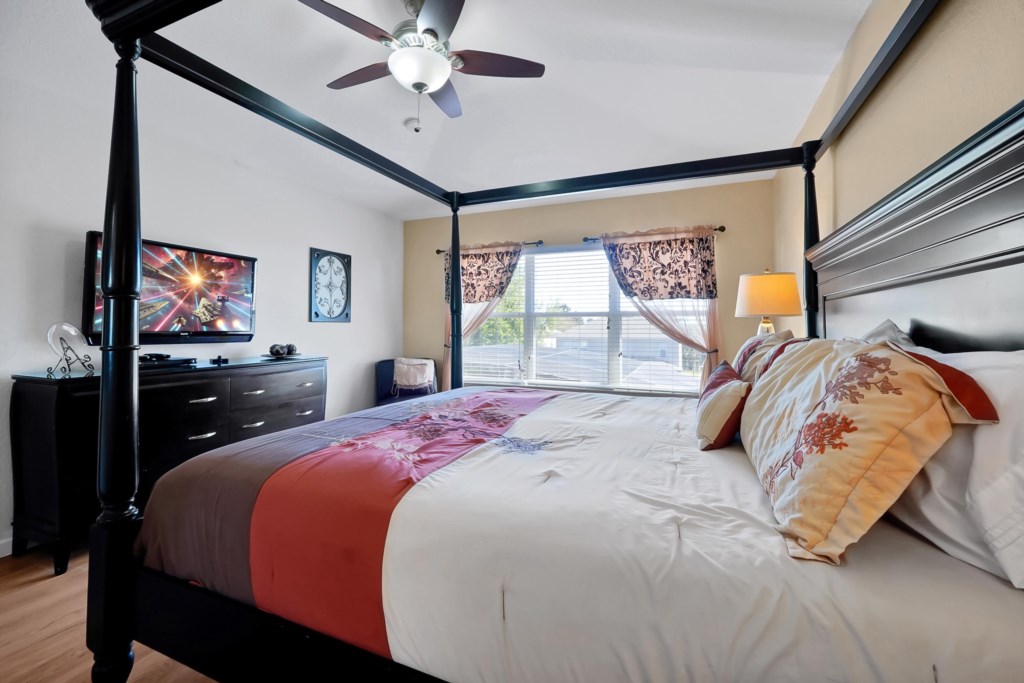 Elegant bedroom with a four-poster bed, flat-screen TV, and natural light from large windows.