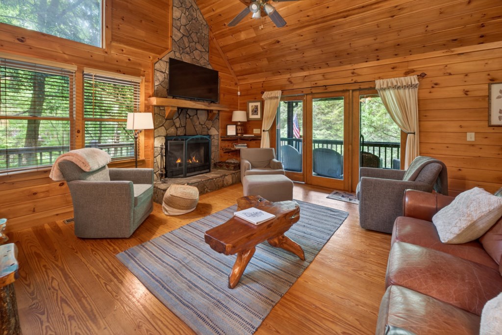 Cozy cabin living room with stone fireplace and forest views from large windows.