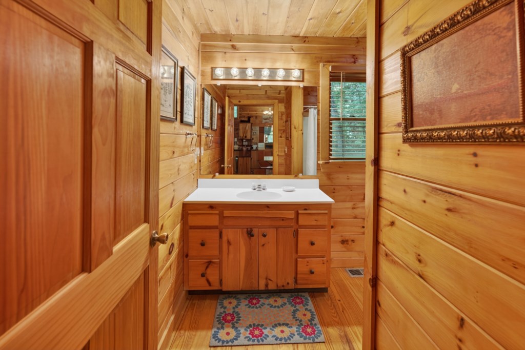 Rustic bathroom with wooden walls and a bright vanity mirror.