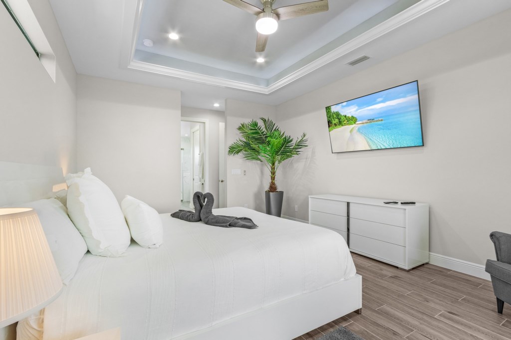 Relax in comfort with a large TV, ceiling fan, and plush bedding in this stylish bedroom.