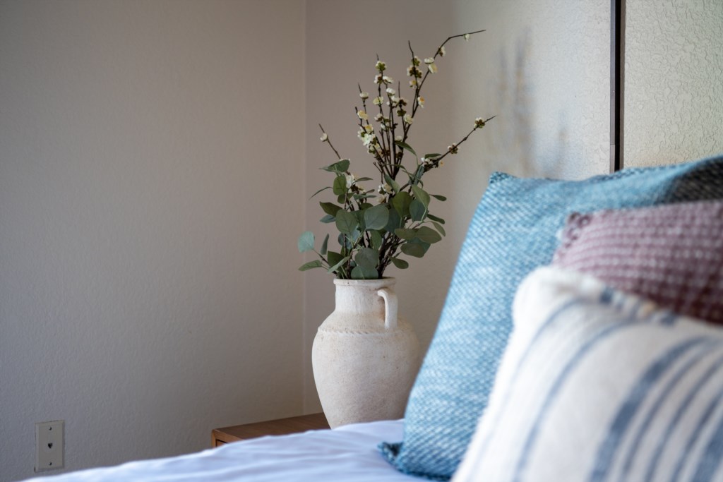 Cozy bedroom corner with decorative vase and plush pillows for a relaxing stay.