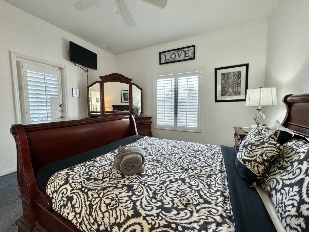 Spacious master bedroom with natural light, TV, and classic wooden furnishings.