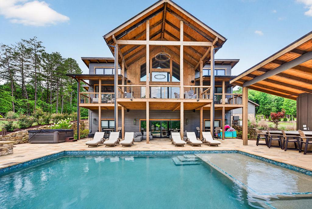 Expansive outdoor pool area with lounge chairs and a scenic wooded backdrop.