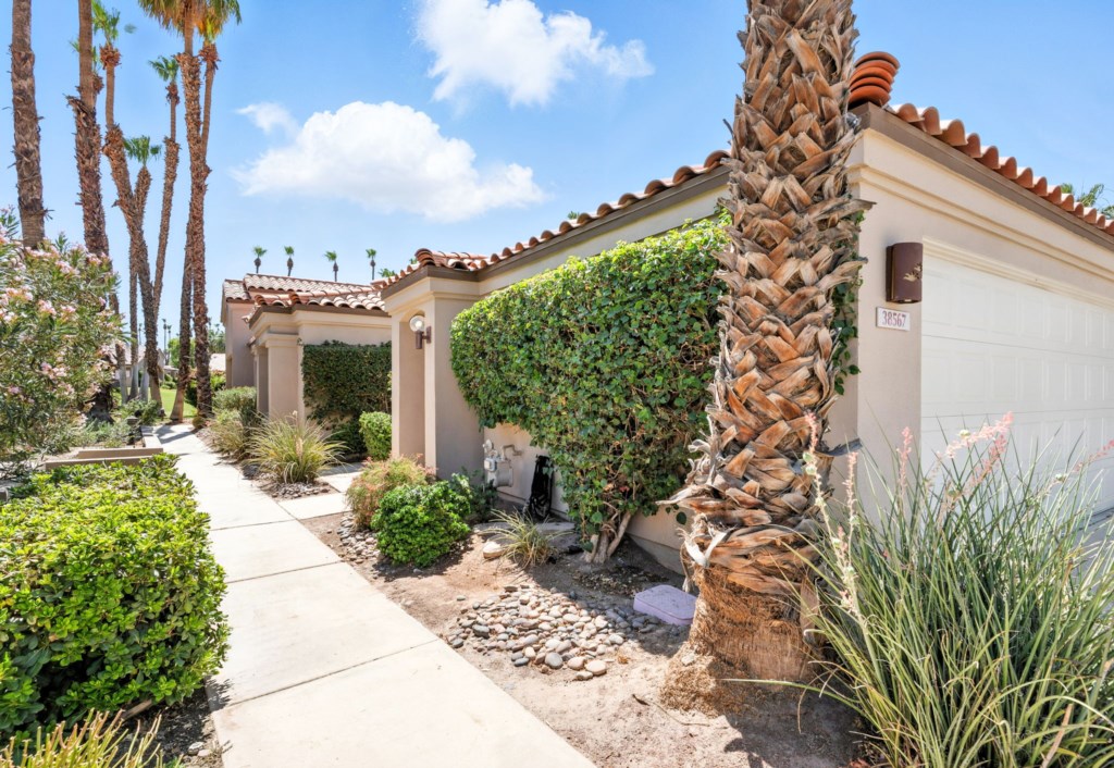 Charming villa entrance flanked by lush gardens and towering palms.