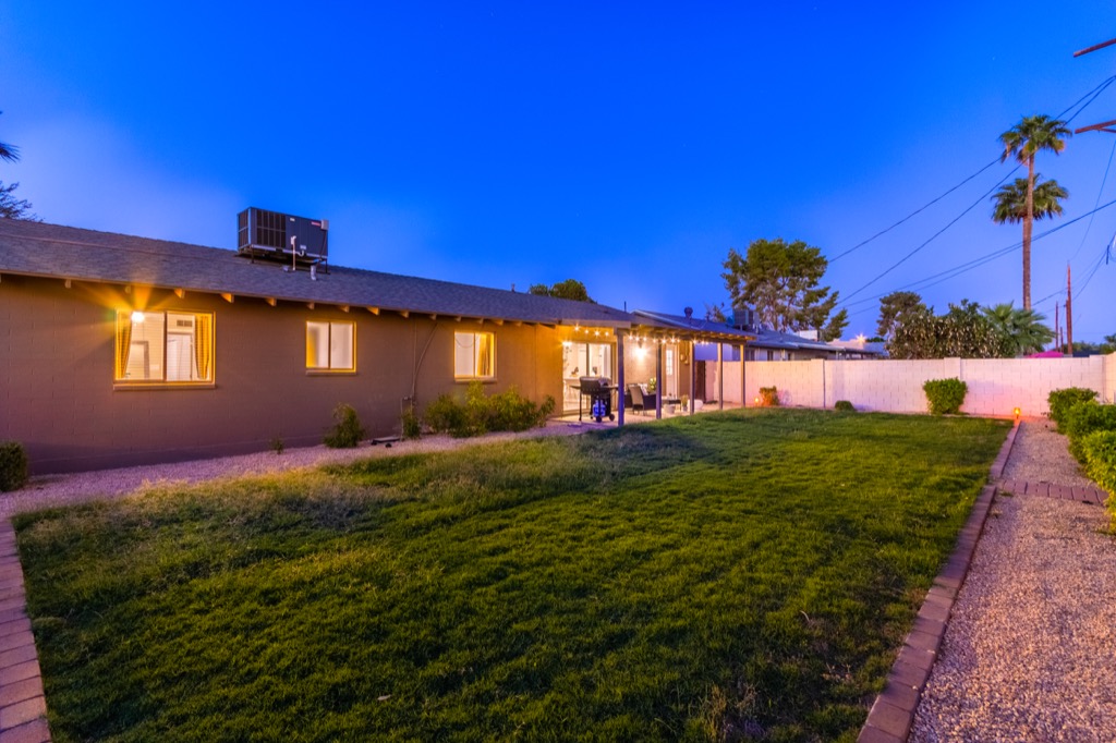 Twilight view of a serene backyard with lush grass and cozy patio seating.
