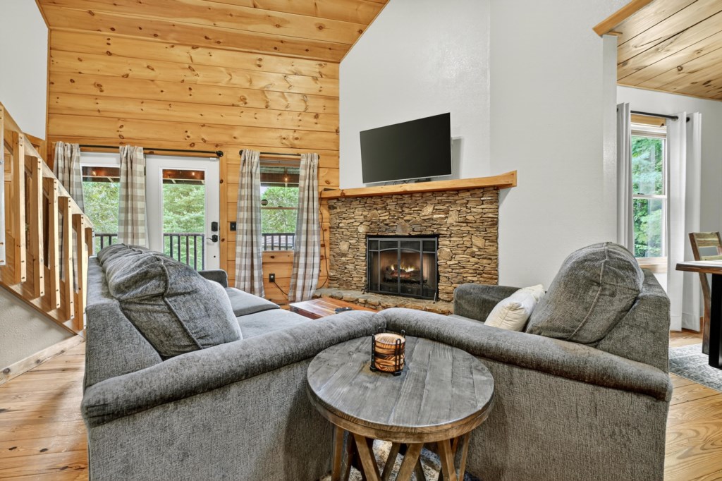 Cozy living room with a stone fireplace and lush forest views.