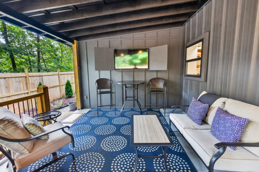 Cozy covered patio with comfy seating and a TV, perfect for outdoor relaxation.