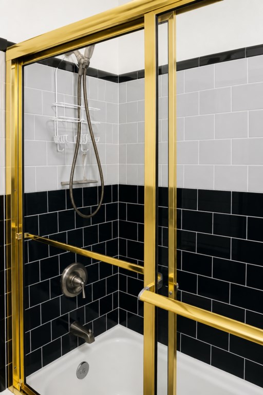 Tiled shower with black-and-white accents and classic brass-framed glass doors.