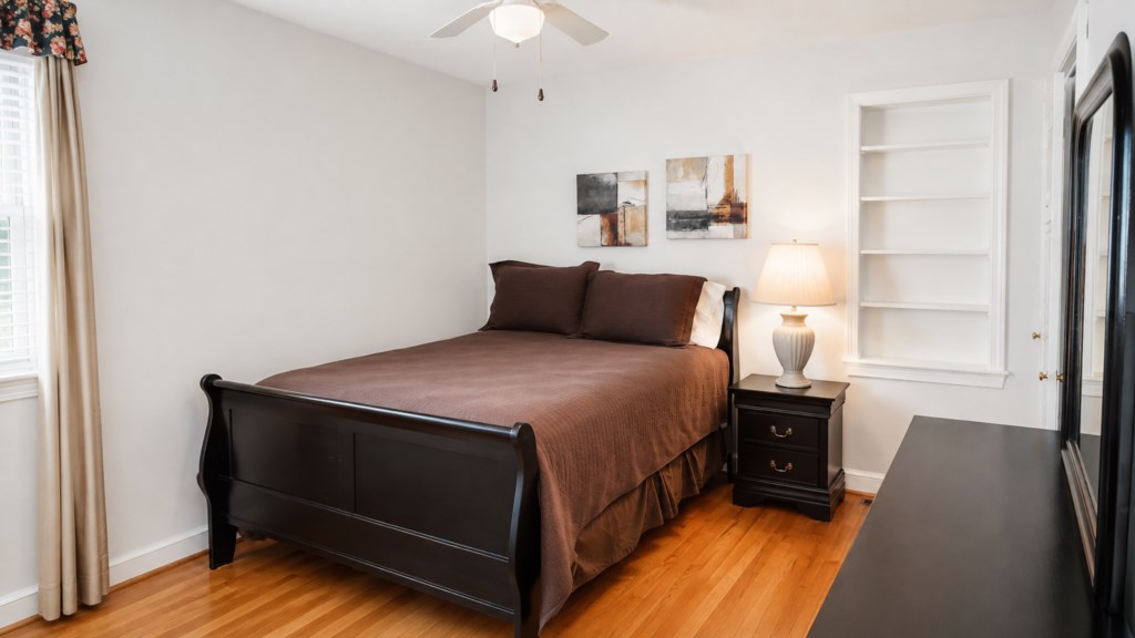 Comfortable queen bedroom with hardwood floors, dresser and built-in shelving.