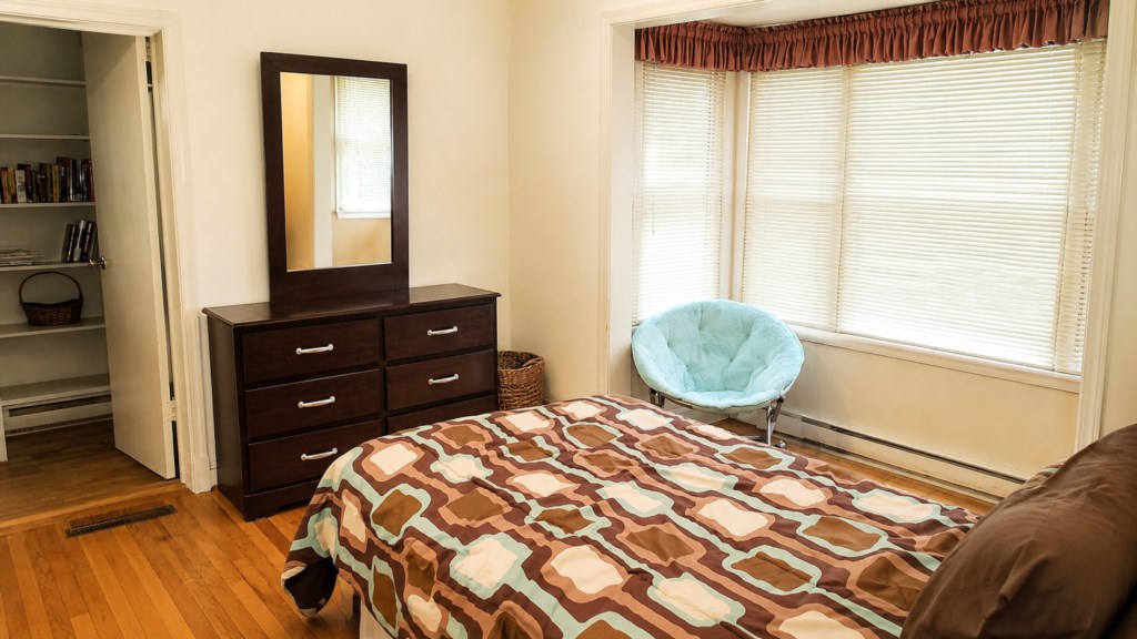 Guest bedroom with bay windows, dresser and cozy seating area.