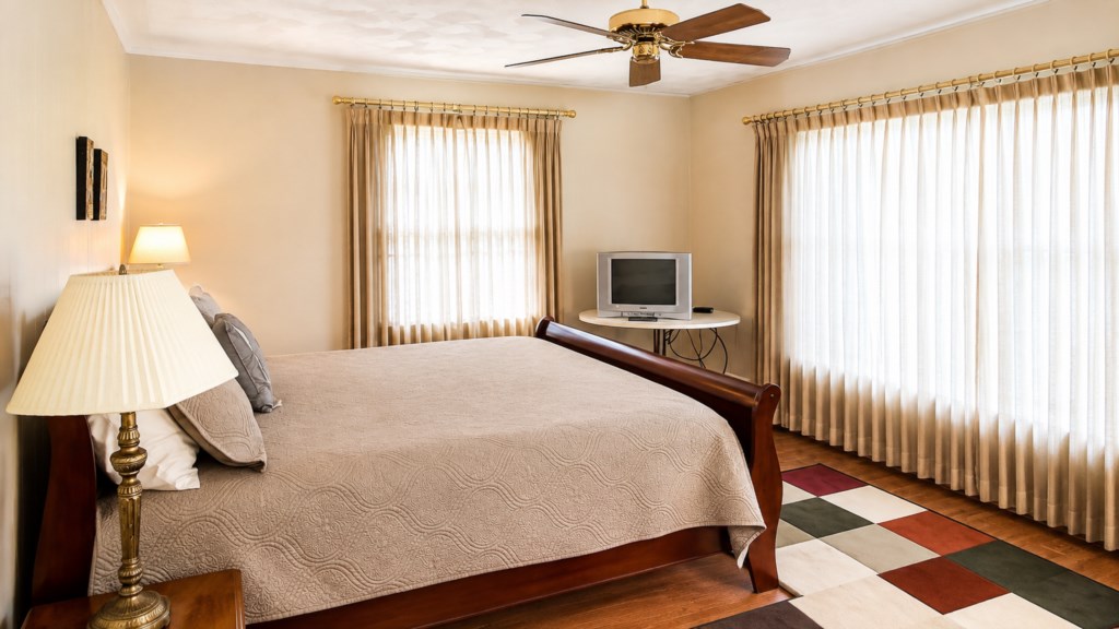 Spacious primary bedroom with large windows, ceiling fan and in-room TV.