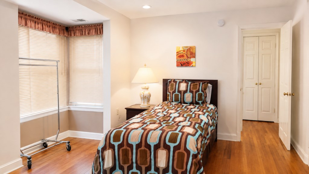 Twin bedroom with bay windows, nightstand and convenient hanging rack.