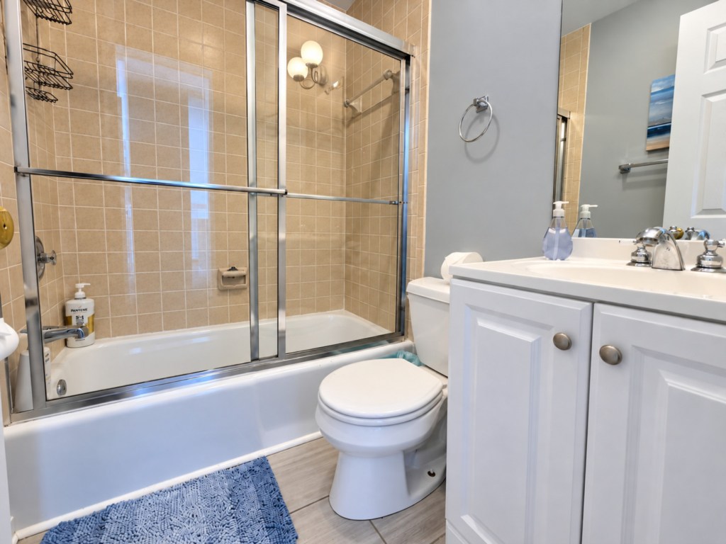 Full bathroom with a tub and glass shower doors. Guests in Twin Room and Queen room share this bath