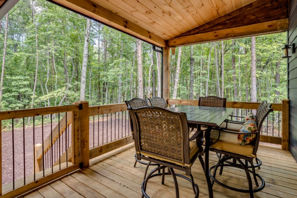 Relax on the covered deck with forest views and comfortable seating for outdoor dining.