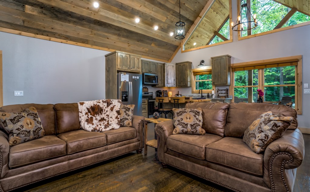 Rustic open-concept living area with cozy seating and a view of the lush forest through large windows.