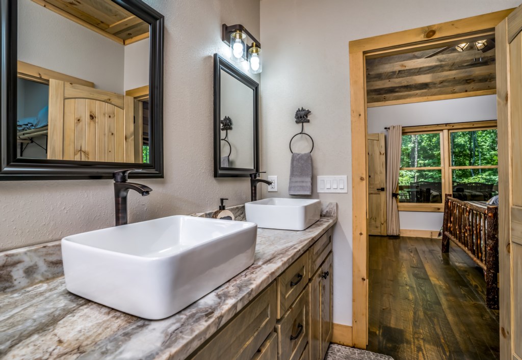 Rustic bathroom with dual sinks and natural wood accents, leading to a cozy bedroom.