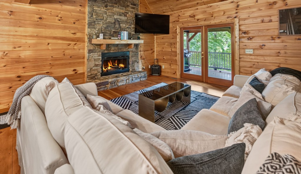 Cozy living room with a stone fireplace and access to a private deck with forest views.