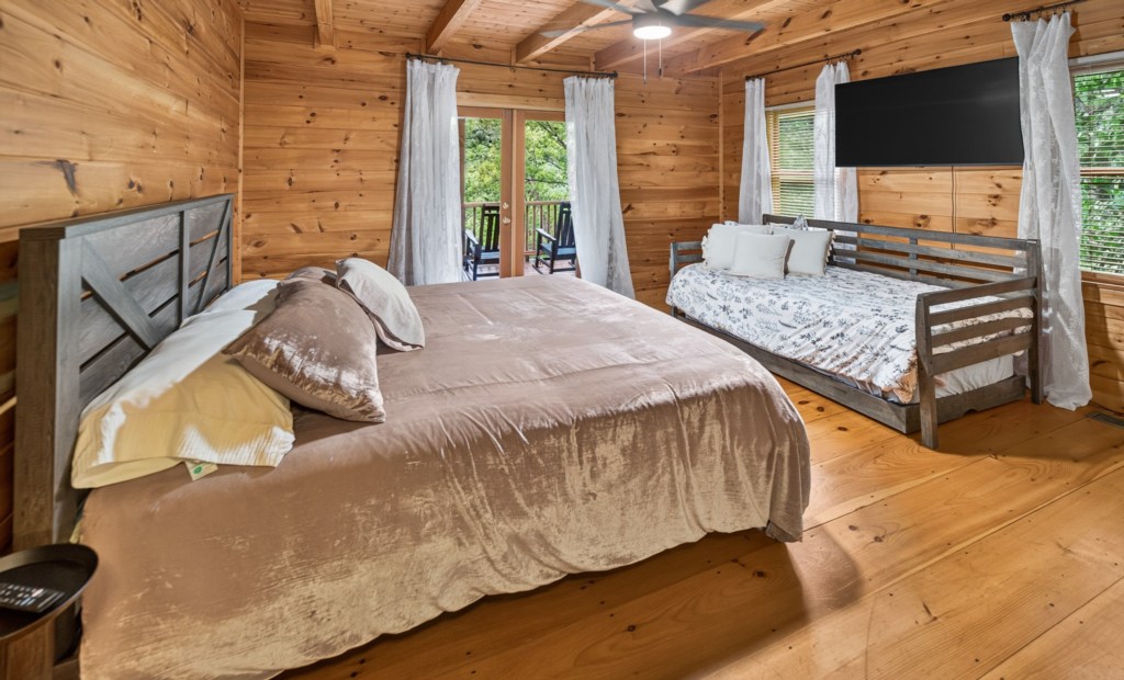 Rustic bedroom with king bed, daybed, and private balcony overlooking lush greenery.