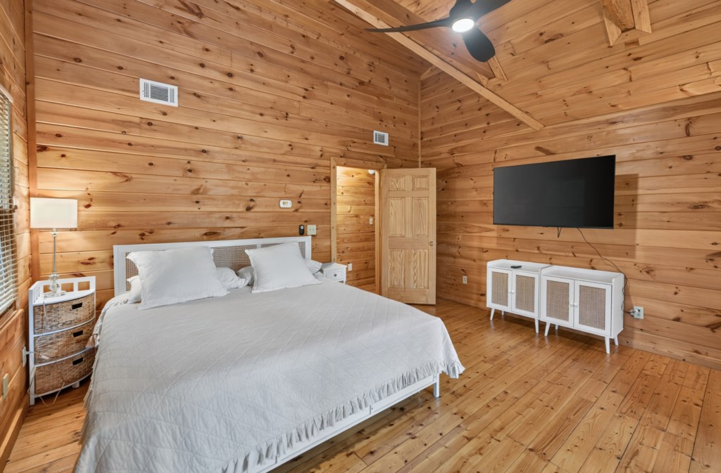 Rustic bedroom with wood paneling, king bed, and wall-mounted TV for cozy relaxation.